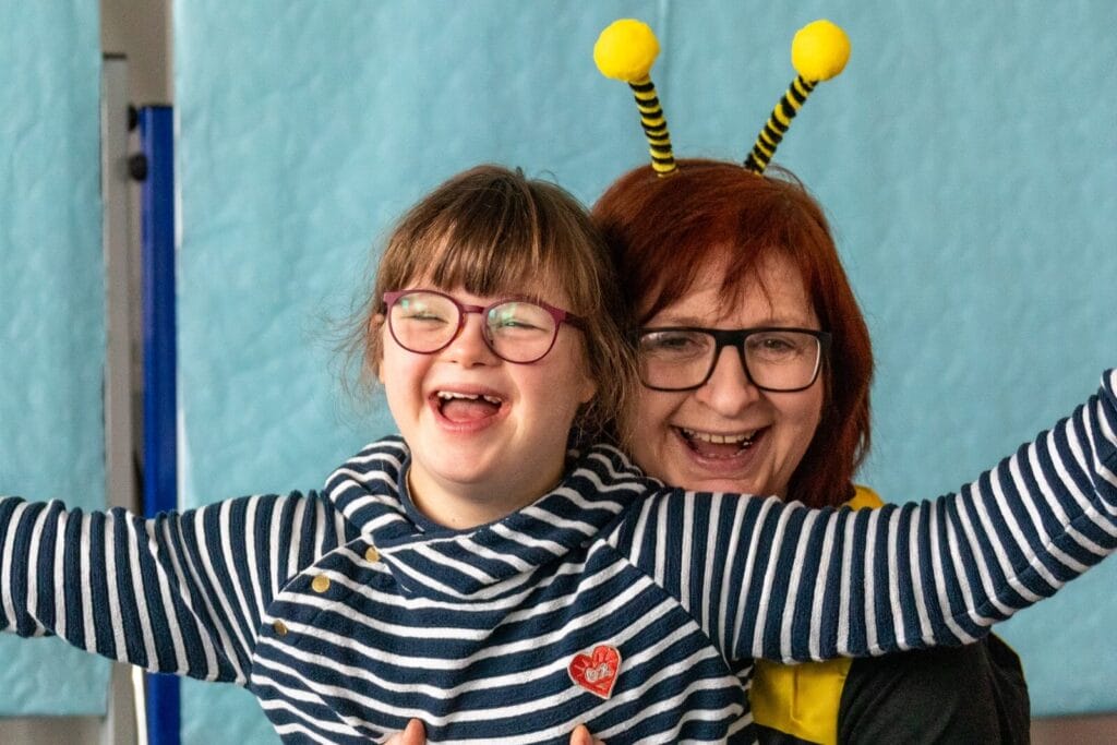 Mädchen mit roter Brille und gestreiftem Pulli zusammen mit einer Erzieherin, die sich als Biene verkleidet hat