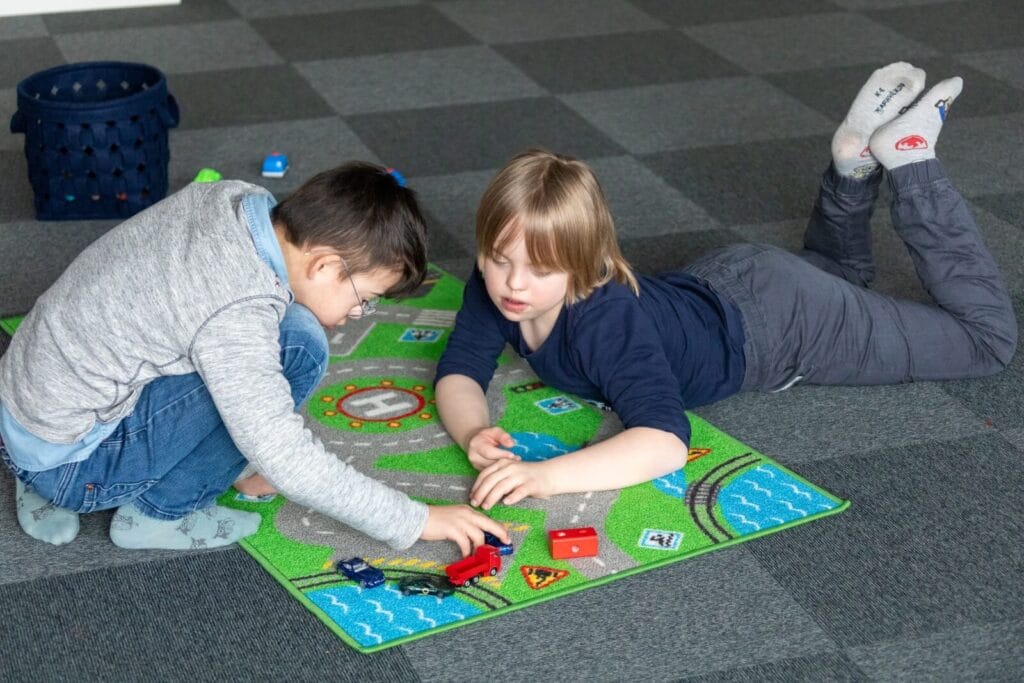 2 Kinder spielen auf Straßenteppich mit Autos