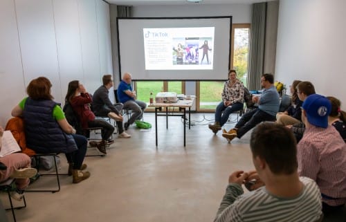 Junior-Tagung einsmehr, viele Menschen sitzen im Kreis bei einem Vortrag