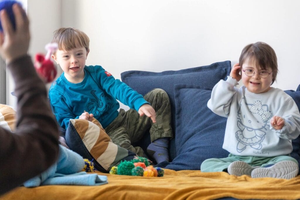 Junge und Mädchen mit Down Syndrom sitzen auf Sofa und werfen Bälle