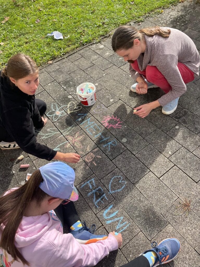 3 Mädchen malen mit bunter Kreide auf ein Pflaster