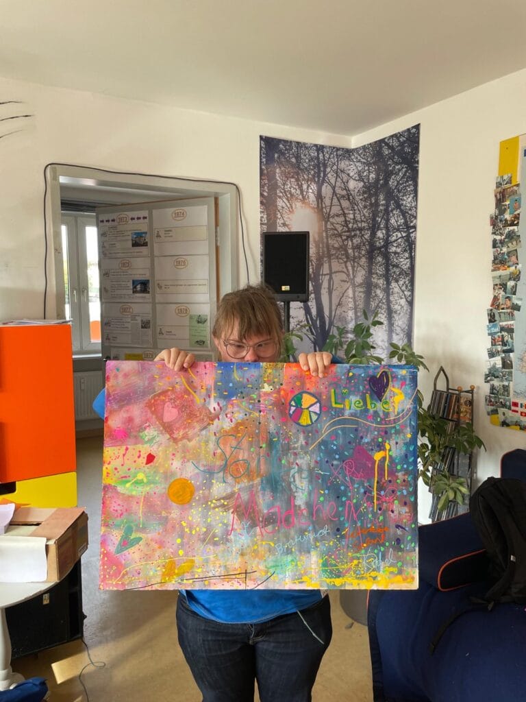 Mädchen zeigt Leinwand mit fröhlichen Farben und Schriftzug "Starke Mädchen"